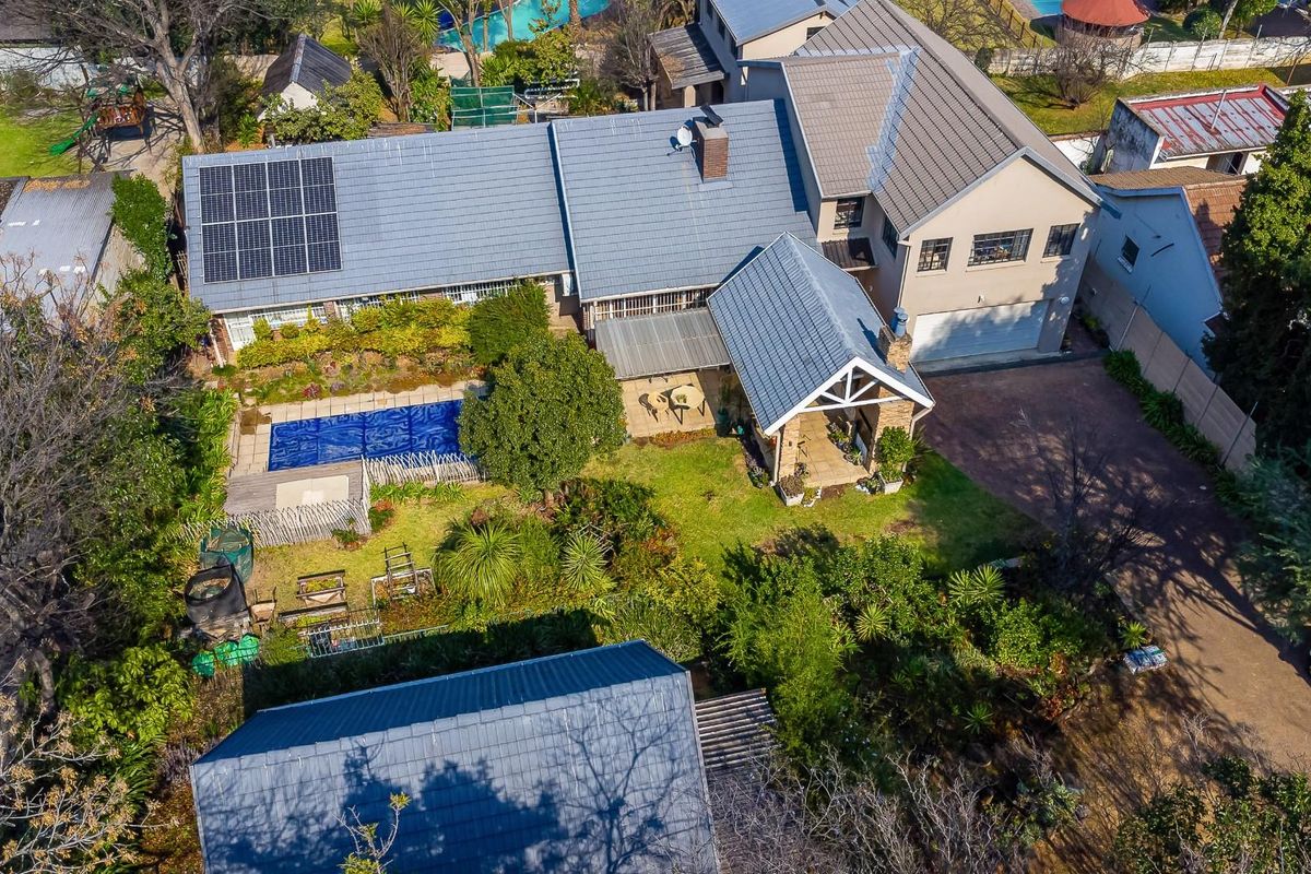 Aerial view of a residential property featuring a tiled roof, solar panels, a swimming pool, a covered patio, and established garden landscaping.