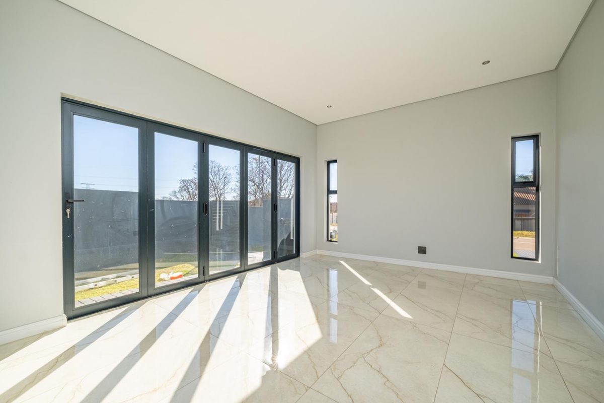 A bright, modern living area featuring large black-framed folding glass doors, sleek marble-look floor tiles, and minimalist neutral walls.