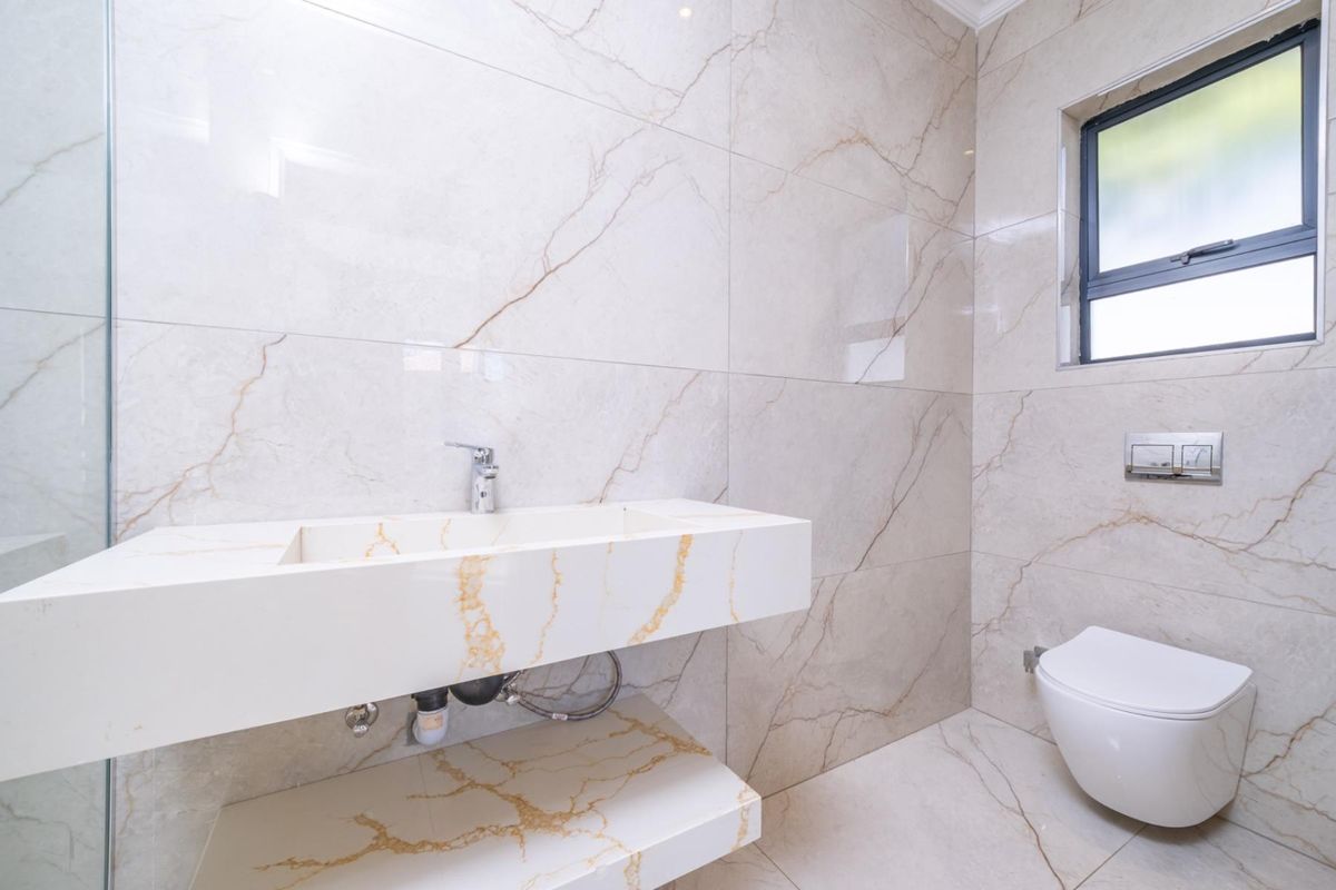 Modern bathroom featuring floor-to-ceiling marble-look tiling, a floating stone vanity with integrated basin, and a wall-mounted toilet with concealed cistern.