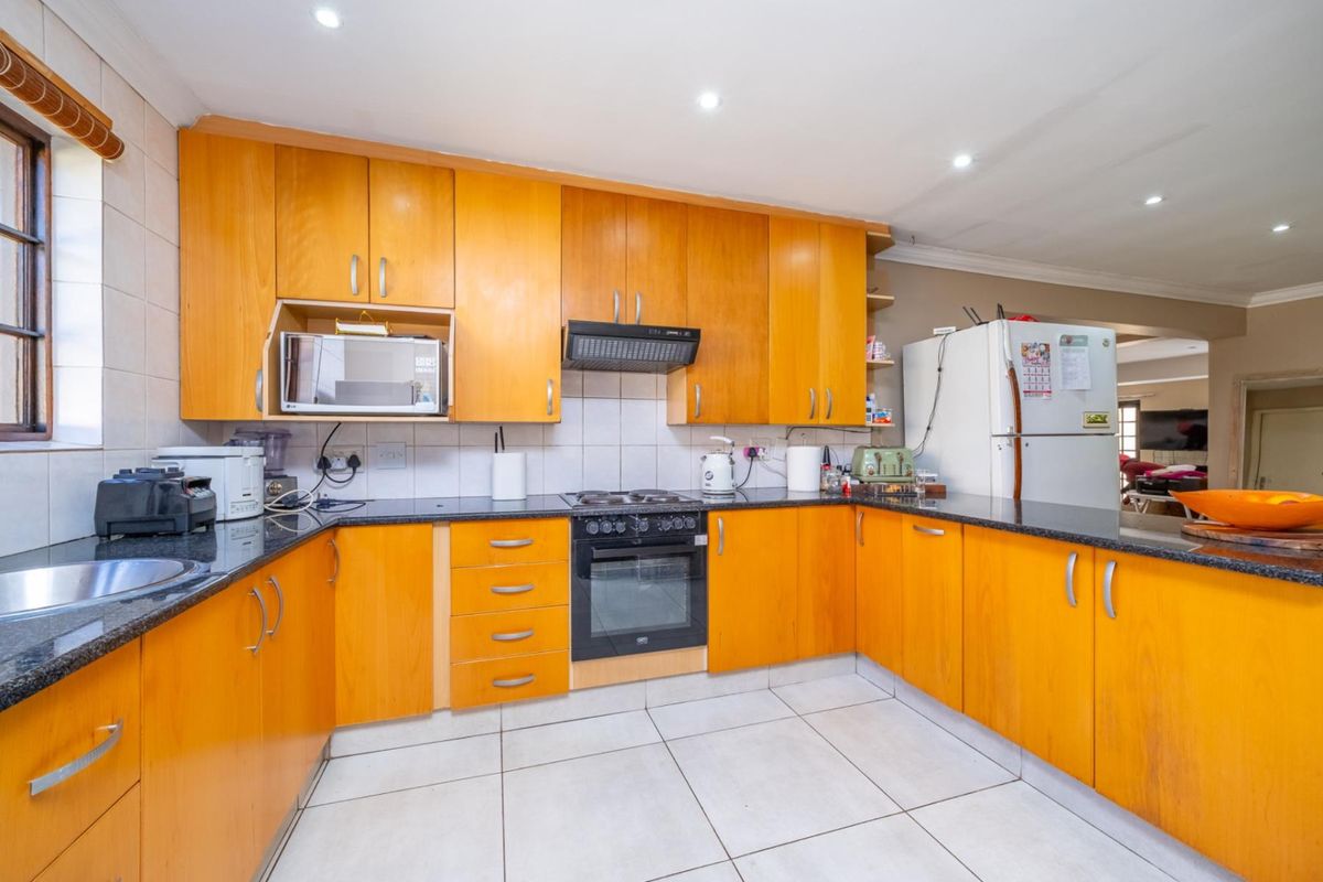 A functional kitchen featuring warm-toned wooden cabinetry, dark granite countertops, built-in oven, extractor fan, and tiled flooring with recessed ceiling lighting.