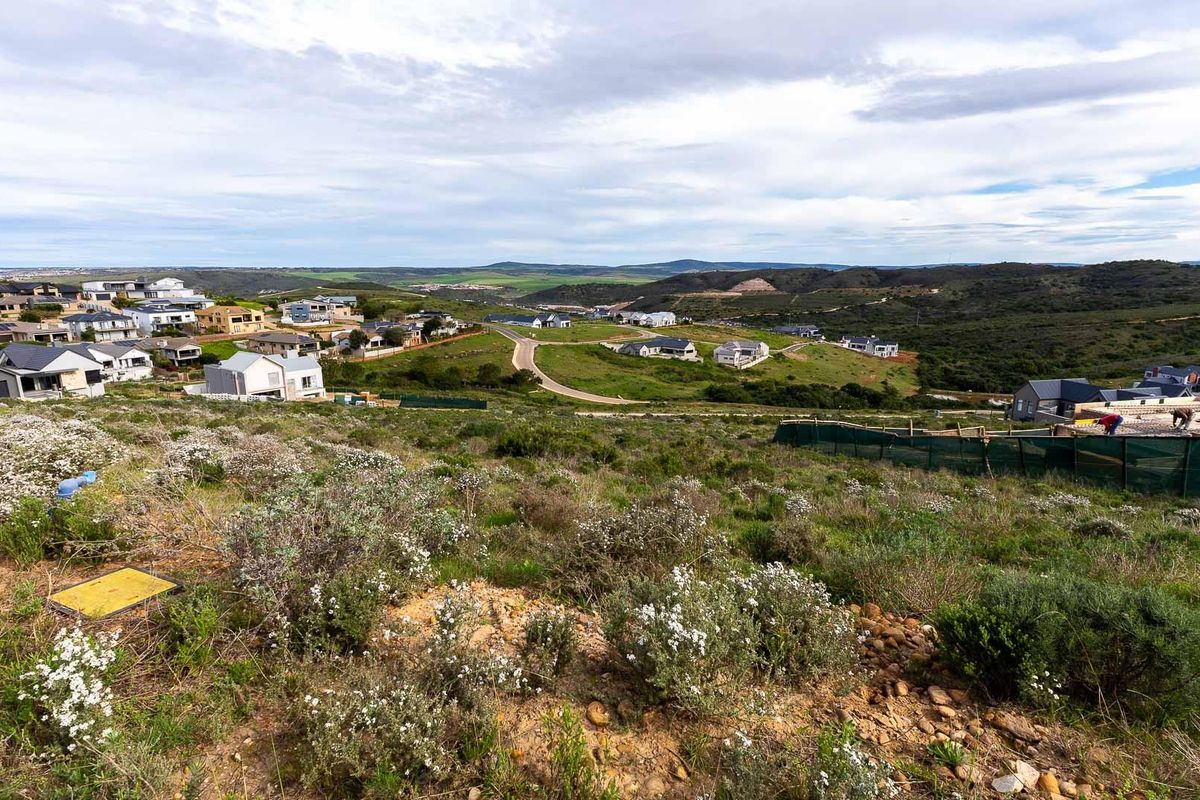 A wide-angle view of a vacant residential plot overlooking a developing estate with rolling hills and surrounding neighborhood infrastructure.