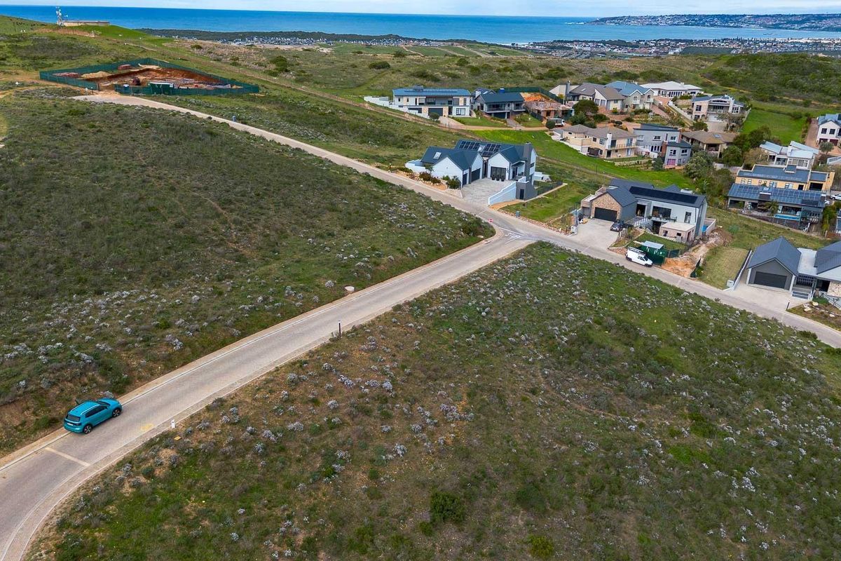 An aerial view of a residential estate featuring vacant land plots, paved roads, and established modern homes with coastal views in the distance.