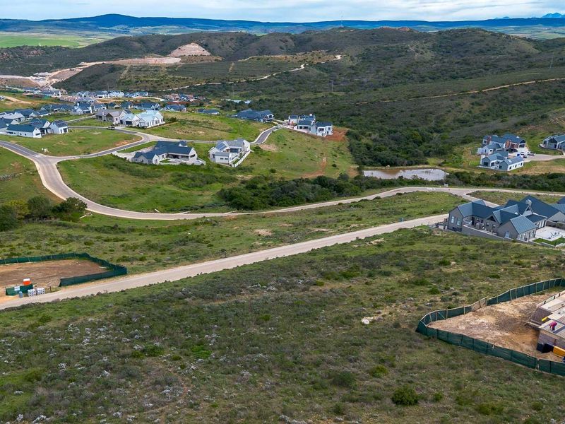An aerial view of a residential estate showing surrounding landscape, paved road infrastructure, and a construction site in the foreground.