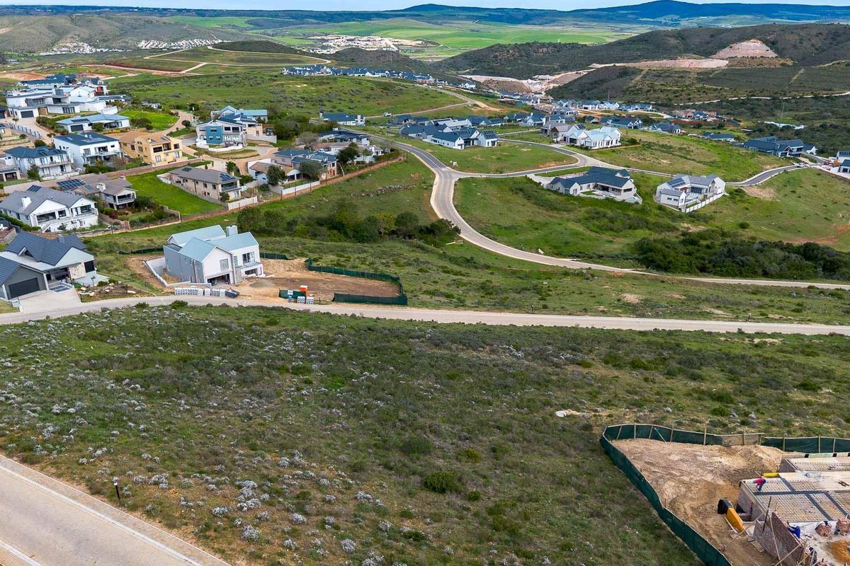 An aerial view of a residential estate featuring vacant land plots, paved roads, and surrounding hillside landscape.