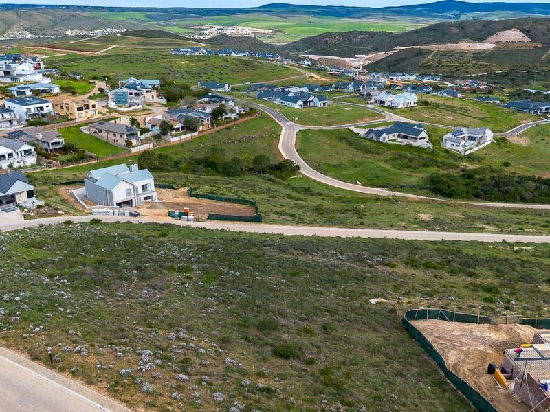 An aerial view of a residential estate featuring vacant land plots, paved roads, and surrounding hillside landscape.