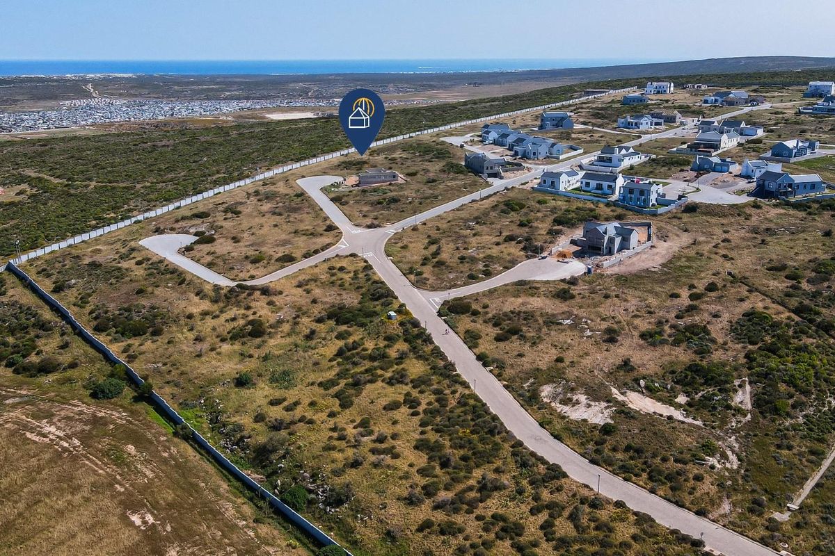 Aerial view of a residential development site featuring paved roads, perimeter fencing, and surrounding coastal landscape.