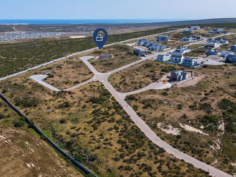Aerial view of a residential development site featuring paved roads, perimeter fencing, and surrounding coastal landscape.