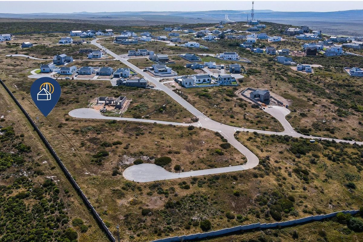 Aerial view of a residential estate featuring vacant plots, paved access roads, and established perimeter fencing in a coastal landscape.