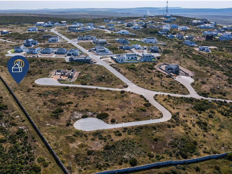Aerial view of a residential estate featuring vacant plots, paved access roads, and established perimeter fencing in a coastal landscape.
