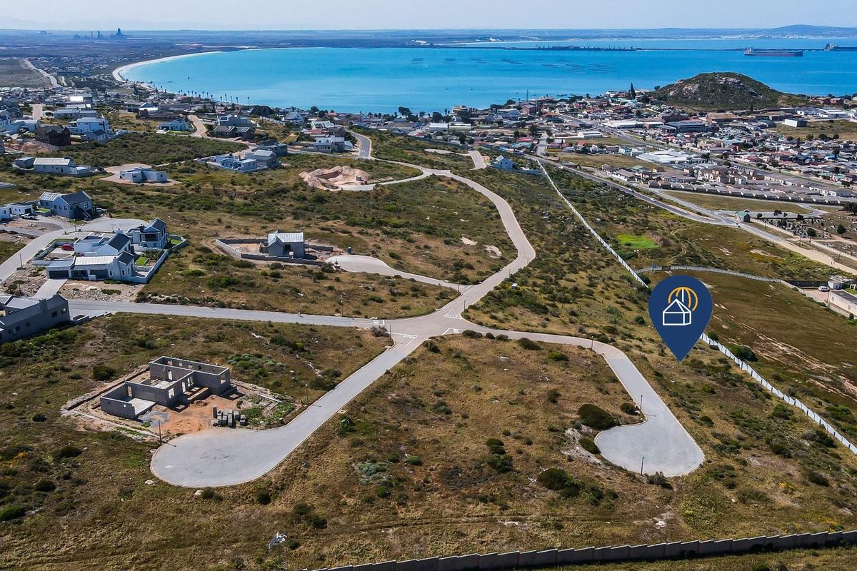 Aerial view of a residential development site featuring paved roads and coastal proximity, showcasing the surrounding neighborhood and landscape.