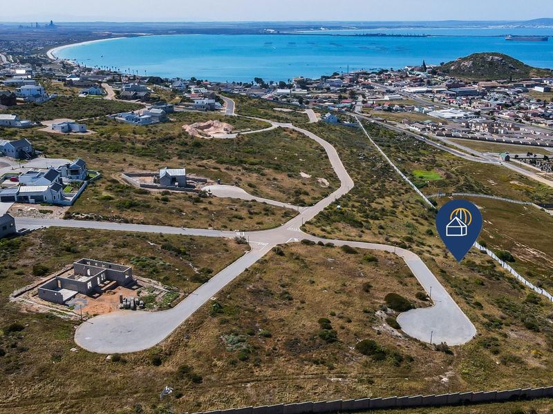 Aerial view of a residential development site featuring paved roads and coastal proximity, showcasing the surrounding neighborhood and landscape.