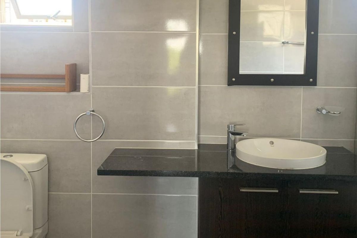 A modern bathroom featuring grey wall tiles, a dark granite vanity countertop with a vessel sink, and a wall-mounted mirror.