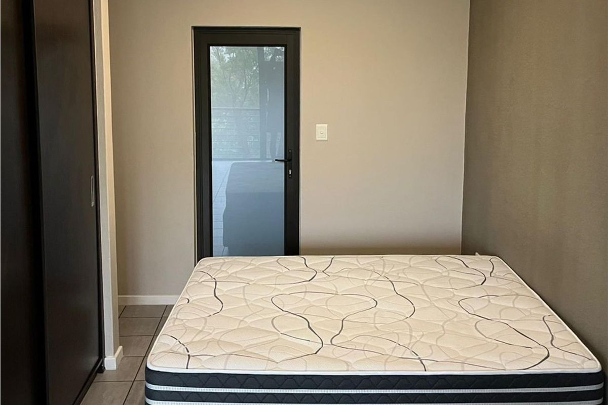 A bedroom featuring neutral wall tones, tiled flooring, a built-in wardrobe, and a glass-panelled door providing access to an outdoor area.
