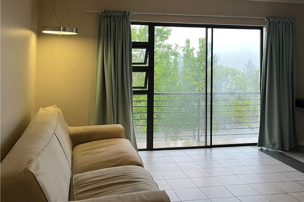 A living area featuring tiled flooring and large sliding glass doors that open onto a balcony with green views.