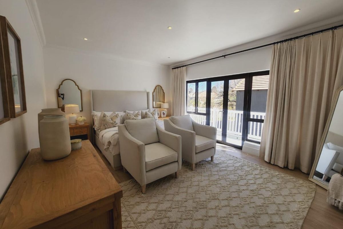 Spacious bedroom featuring light timber flooring, recessed ceiling lighting, and large black-framed glass doors opening onto a private balcony.