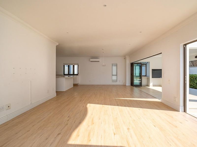Spacious open-plan living area featuring light laminate flooring, recessed lighting, and seamless flow to an outdoor patio through large sliding glass doors.