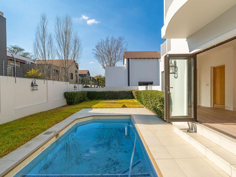 A well-maintained rear garden featuring a swimming pool, tiled patio area, and secure boundary walls with electric fencing, accessible via bi-fold doors.