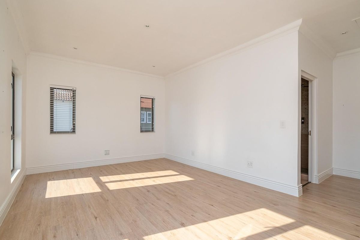A bright, vacant bedroom featuring light-toned laminate flooring, crisp white walls, recessed lighting, and fitted venetian blinds.