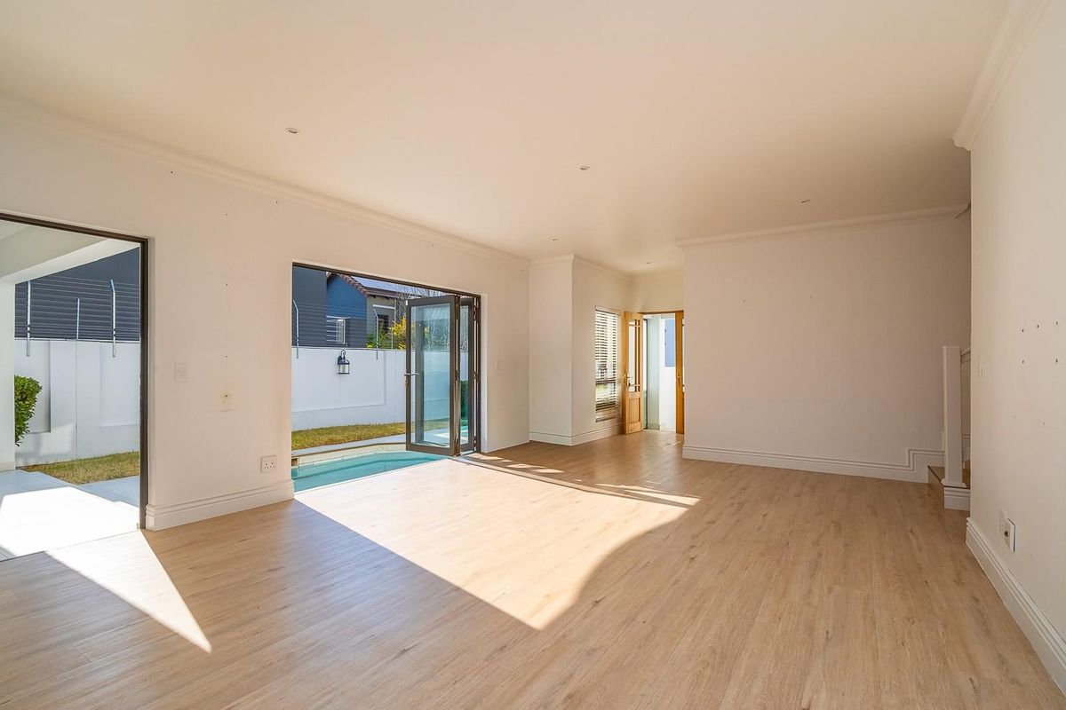 Spacious, light-filled living area featuring modern laminate flooring, recessed lighting, and seamless indoor-outdoor flow through bi-fold doors leading to the patio and pool area.