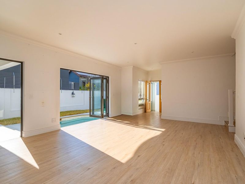 Spacious, light-filled living area featuring modern laminate flooring, recessed lighting, and seamless indoor-outdoor flow through bi-fold doors leading to the patio and pool area.