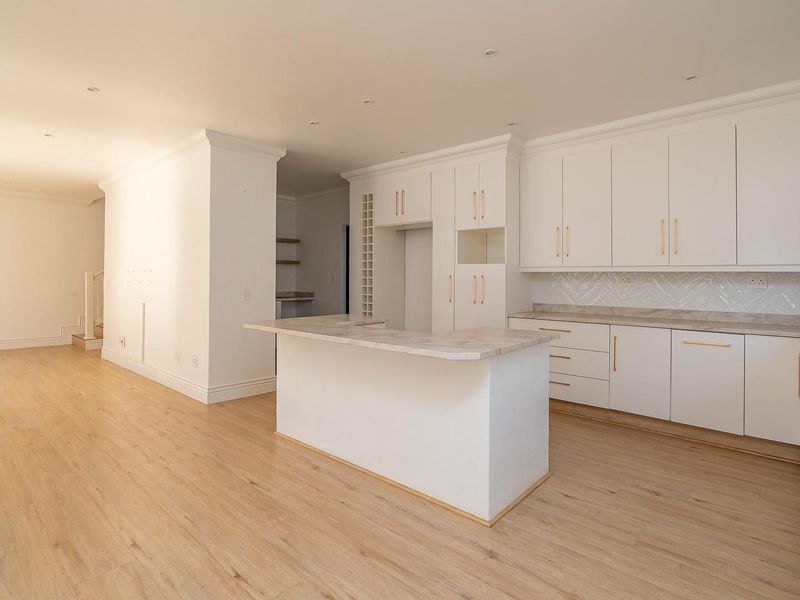 A bright, modern open-plan kitchen featuring white cabinetry, stone countertops, and light wood-look flooring, offering a clean and versatile space.