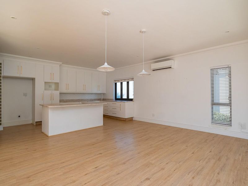 Spacious open-plan kitchen and living area featuring modern white cabinetry, a central island, laminate flooring, and split-system air conditioning.