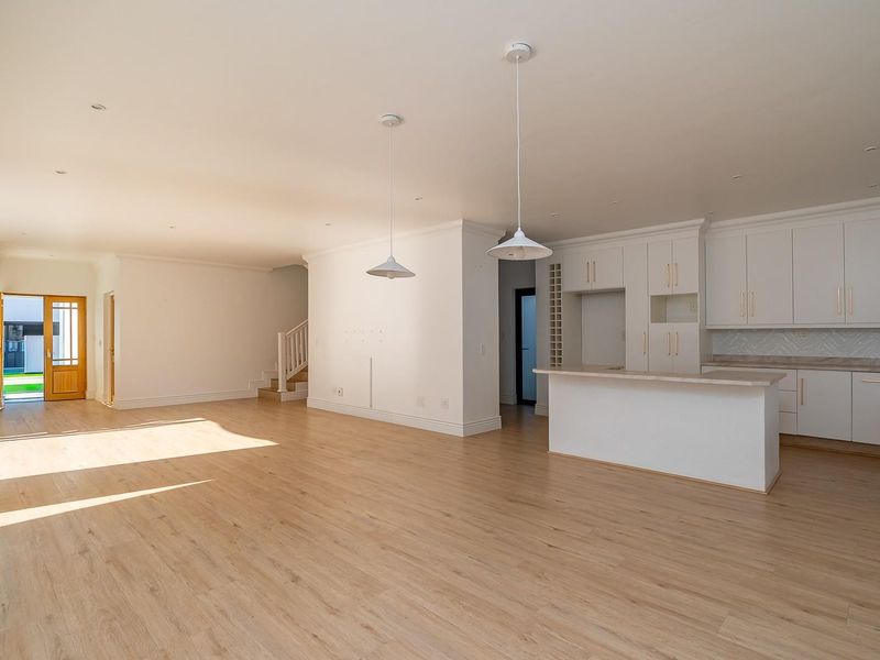 Spacious open-plan living and kitchen area featuring modern white cabinetry, a central island, light wood-look flooring, and abundant natural light.