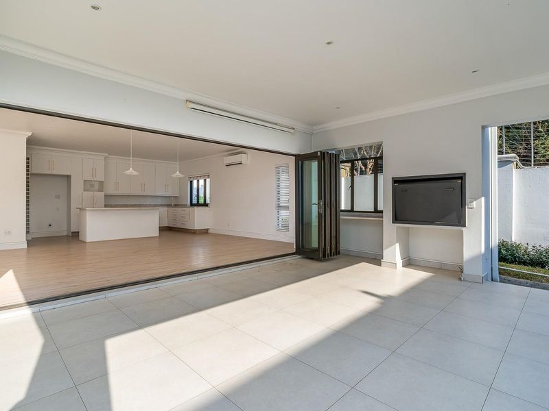 Spacious open-plan living area featuring a modern kitchen with island, seamless indoor-outdoor flow through stacking doors to a tiled patio with built-in braai.