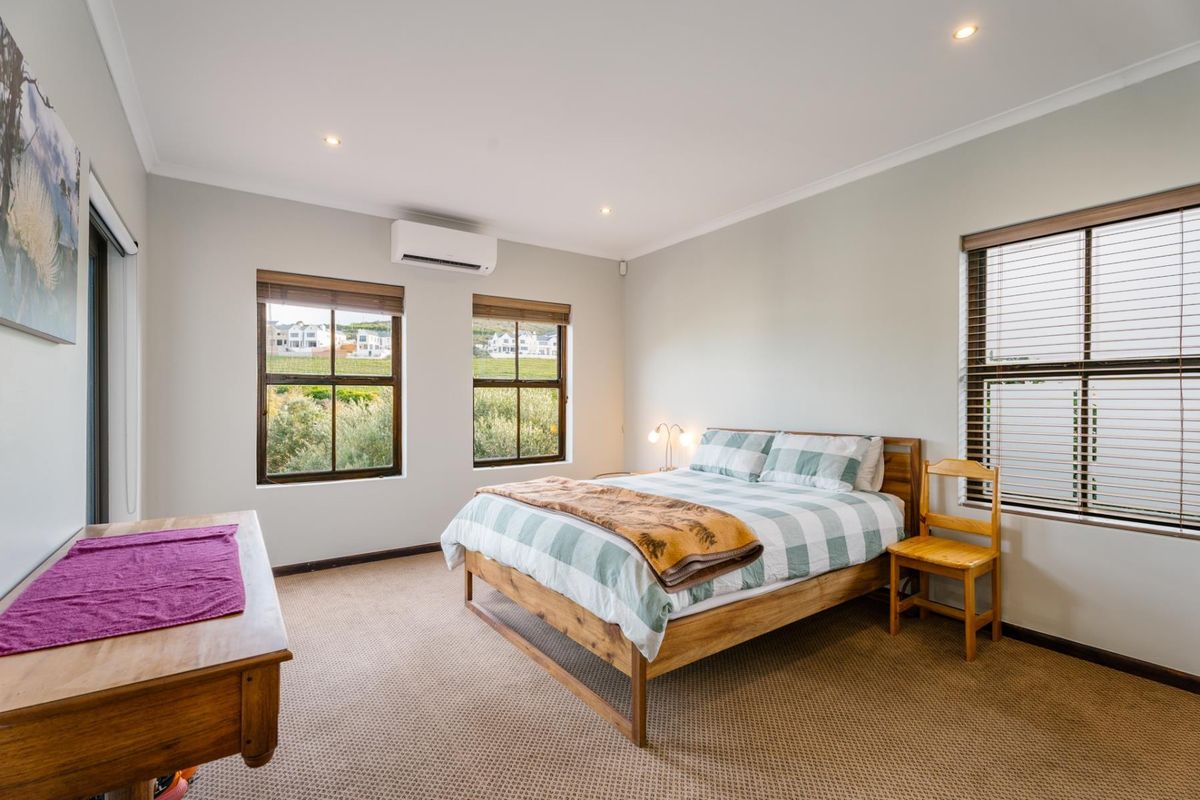 A well-lit bedroom featuring neutral walls, carpeted flooring, recessed downlights, and an integrated air conditioning unit with views through multiple windows.