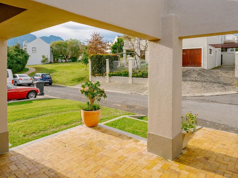 A covered patio area with brick paving and concrete pillars, offering an open view of the street and surrounding residential neighbourhood.