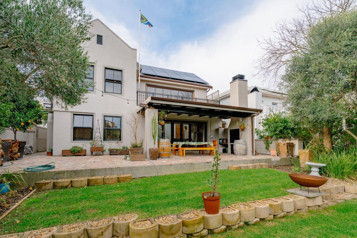 Rear view of the house featuring a covered patio with built-in braai, paved terrace, balcony, and solar panels on the roof.