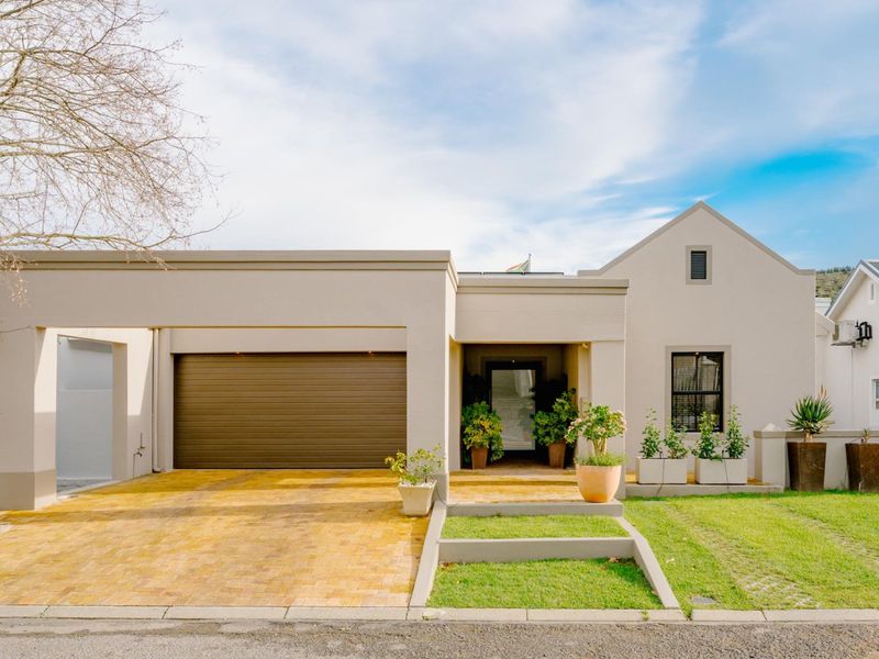 A well-maintained modern front facade featuring a paved driveway, automated garage, and a welcoming covered entrance with landscaped garden elements.