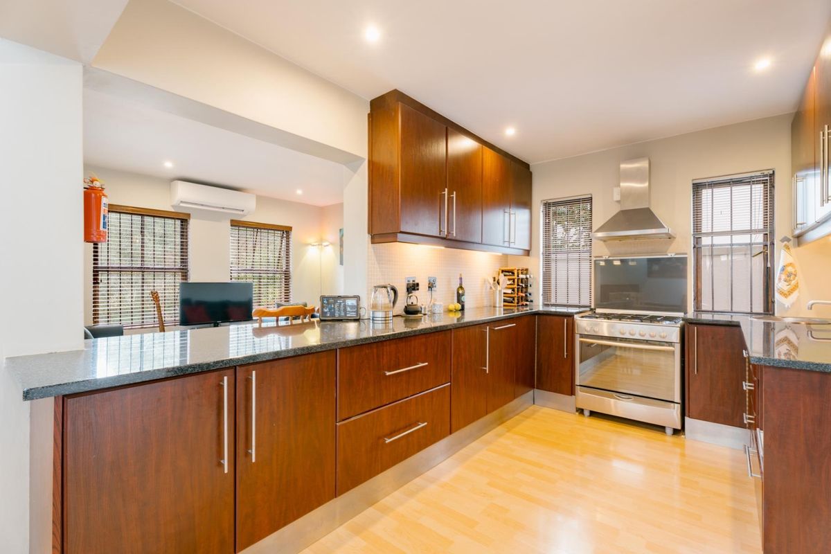 Modern kitchen featuring dark wood cabinetry, granite countertops, and stainless steel appliances, seamlessly flowing into an adjacent living area with air conditioning.