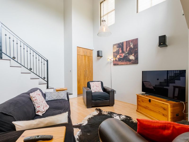 Spacious living room featuring high ceilings, laminate flooring, a wrought iron staircase railing, and a built-in wooden storage cupboard.