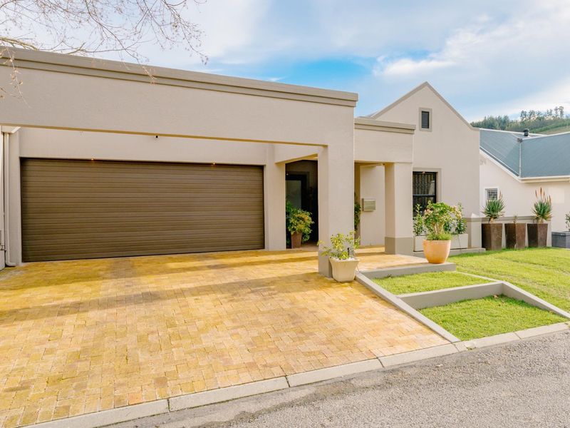 Modern front elevation featuring a paved driveway, automated garage, and well-maintained landscaped garden area.