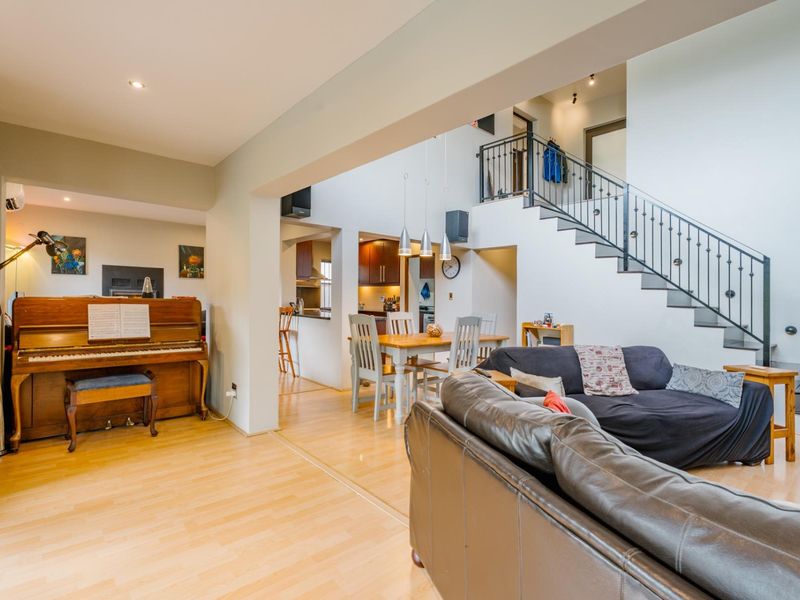 Spacious open-plan living and dining area featuring laminate flooring, a striking wrought iron staircase, and a seamless flow into the kitchen space.