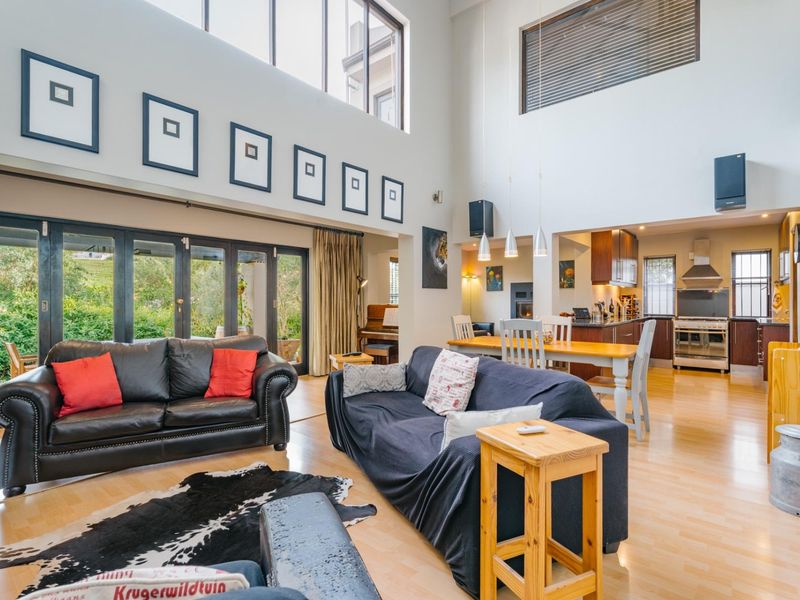 Spacious open-plan living and dining area featuring double-volume ceilings, hardwood floors, and seamless flow to the outdoor patio through large bi-fold glass doors.