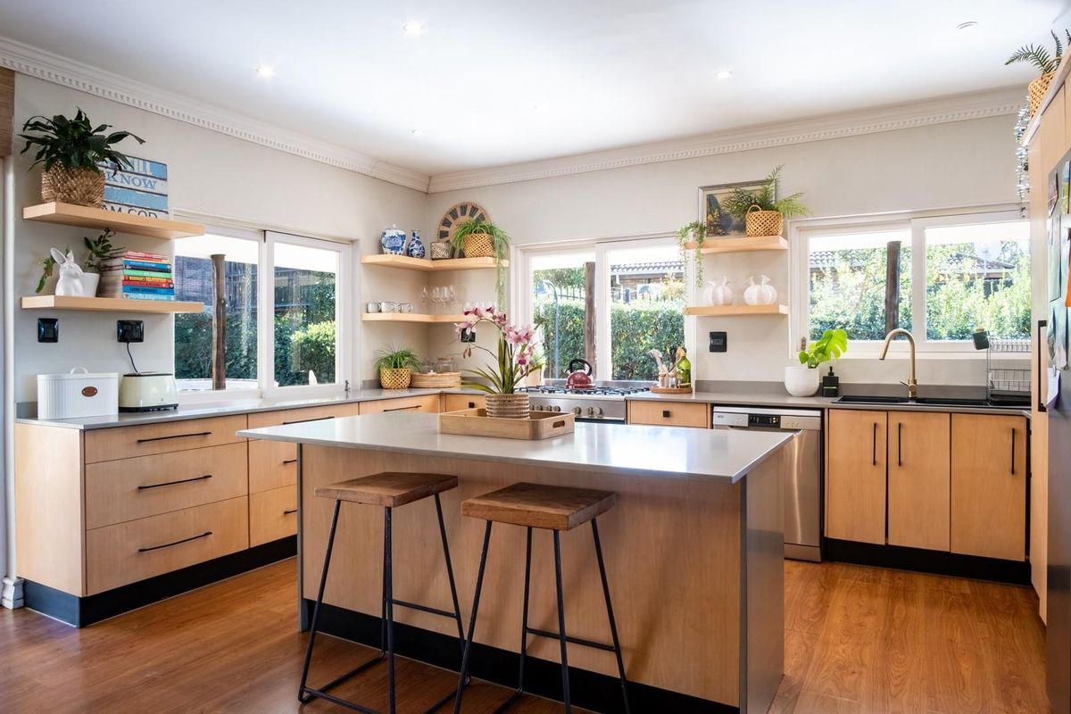 Modern kitchen featuring light wood cabinetry, a central island with a stainless steel countertop, integrated appliances, and large windows overlooking the garden.