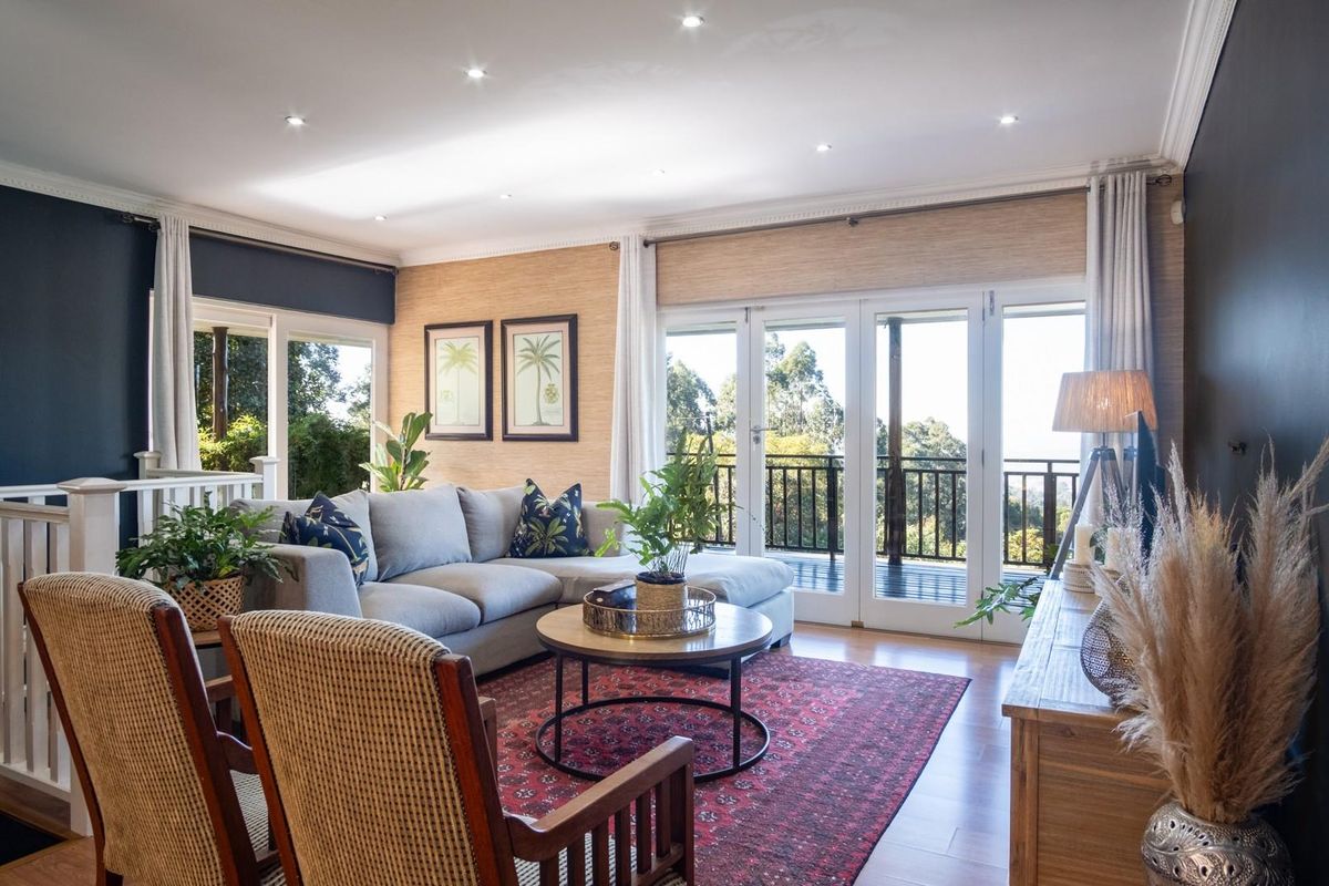 A bright and inviting living room featuring timber flooring, recessed downlighting, and double glass doors opening onto a balcony with scenic views.