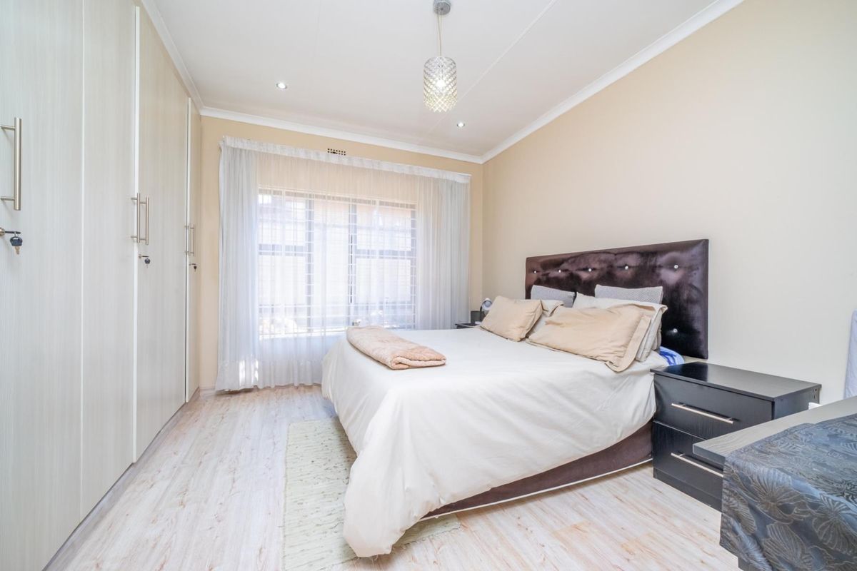 A well-maintained bedroom featuring built-in floor-to-ceiling wardrobes, light wood-look flooring, and recessed ceiling lighting.