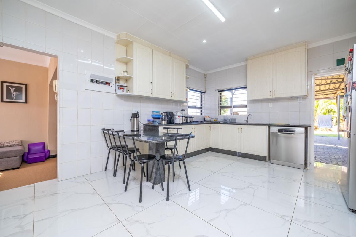 A functional kitchen featuring white cabinetry, granite countertops, tiled flooring, and a built-in dishwasher, with direct access to an outdoor patio area.