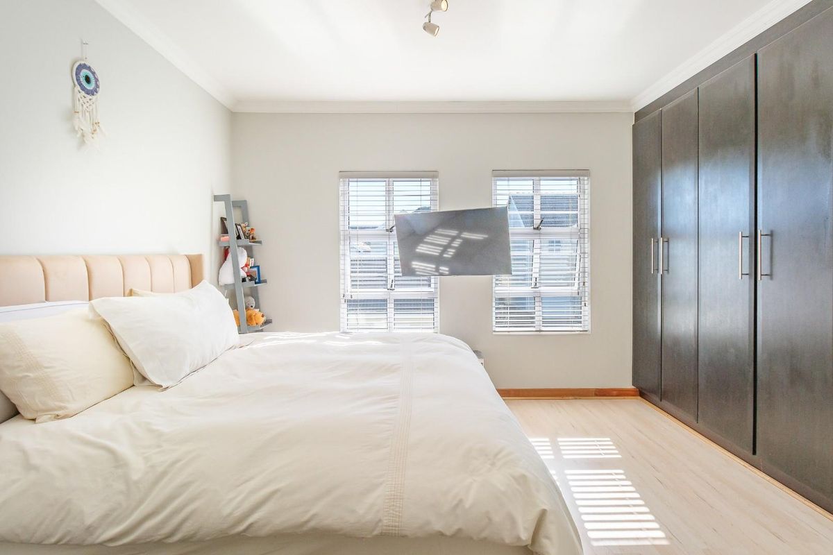A well-maintained bedroom featuring light laminate flooring, neutral walls, built-in dark cabinetry, and dual windows with fitted venetian blinds.