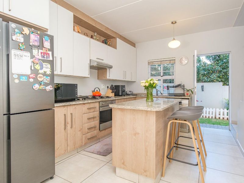 Modern kitchen featuring light wood-tone cabinetry, granite countertops, a central island with breakfast bar seating, and direct access to the rear outdoor area.