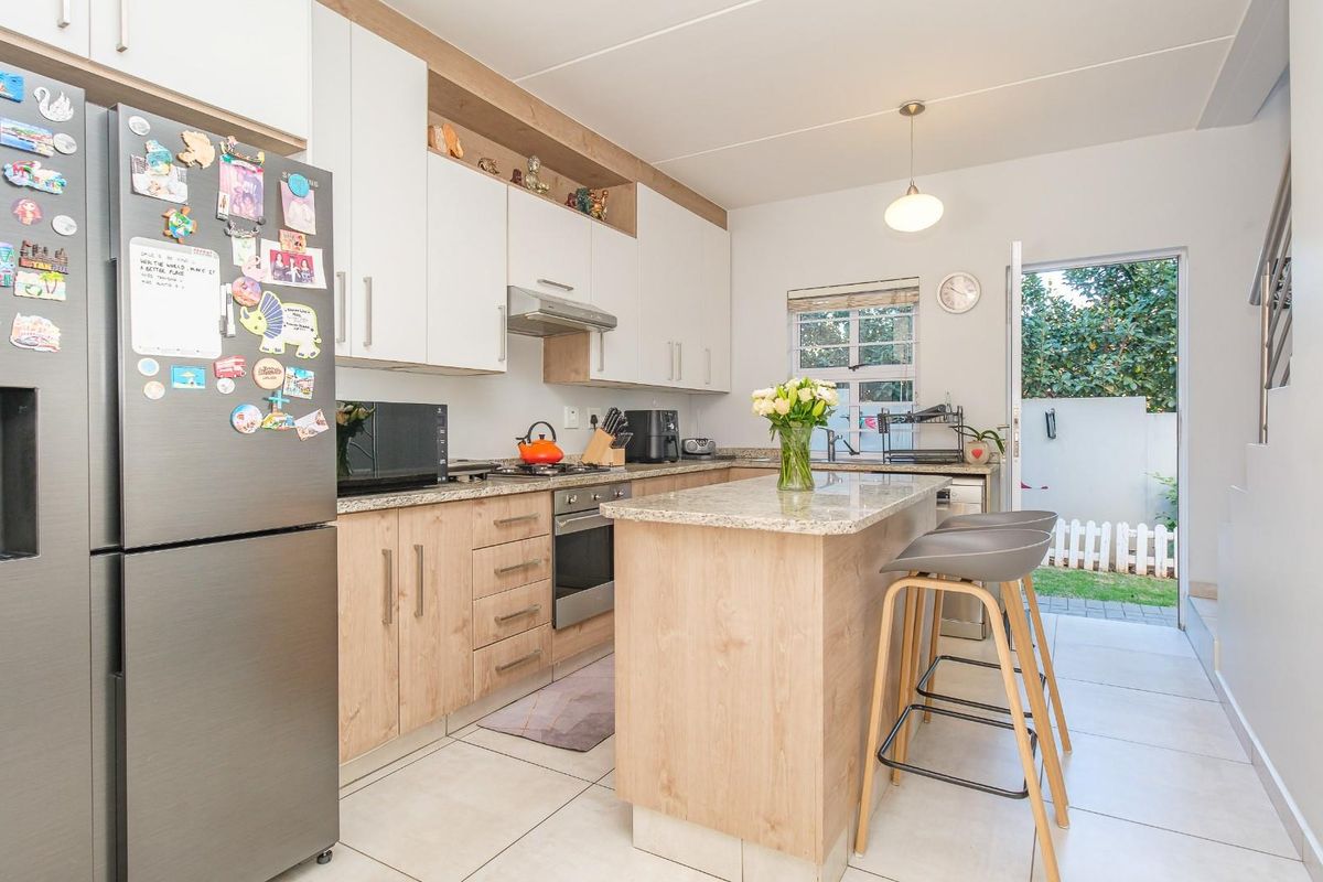 Modern kitchen featuring light wood-tone cabinetry, granite countertops, a central island with breakfast bar seating, and direct access to the rear outdoor area.