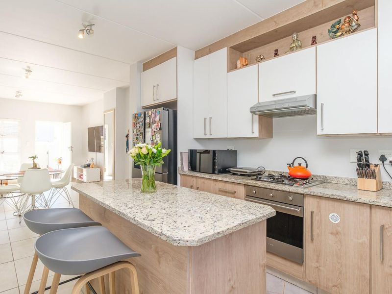 Modern open-plan kitchen featuring granite countertops, light wood cabinetry, and a functional island, seamlessly flowing into the adjacent dining and living area.