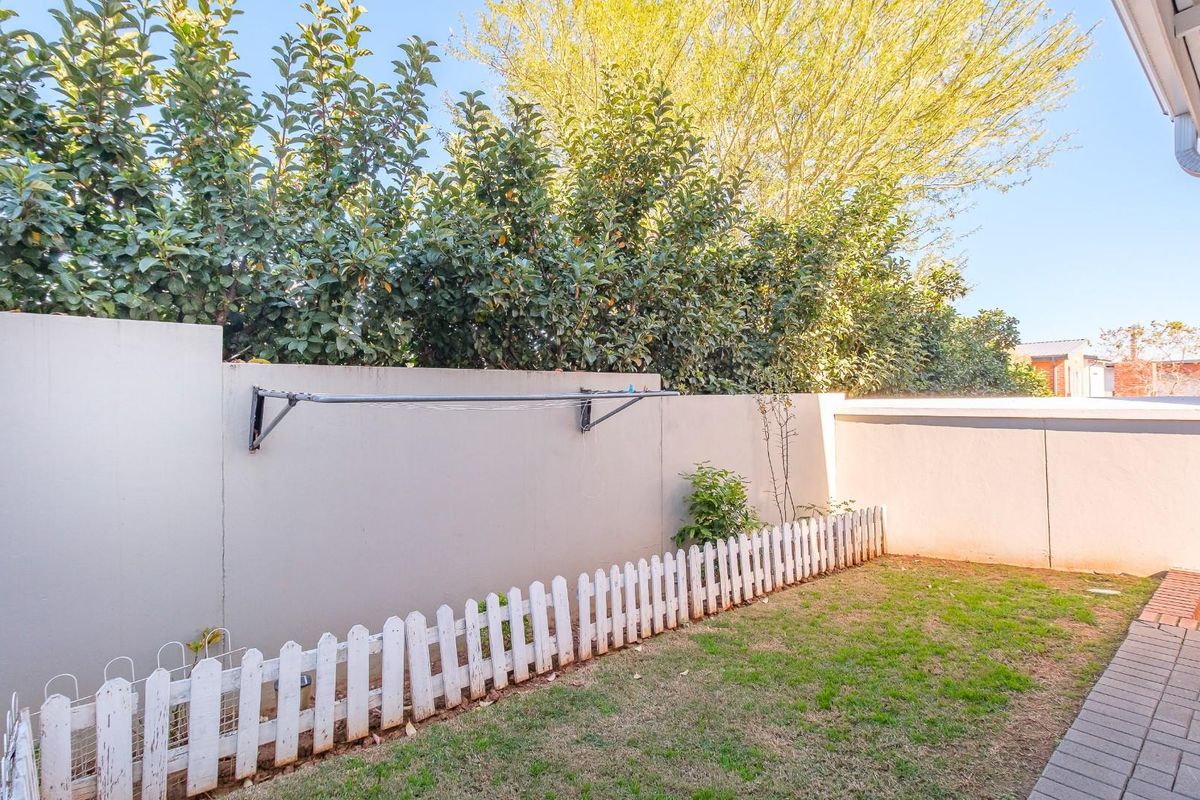 A private rear garden area featuring a paved walkway, a small lawn, and a wall-mounted clothesline against a high boundary wall.