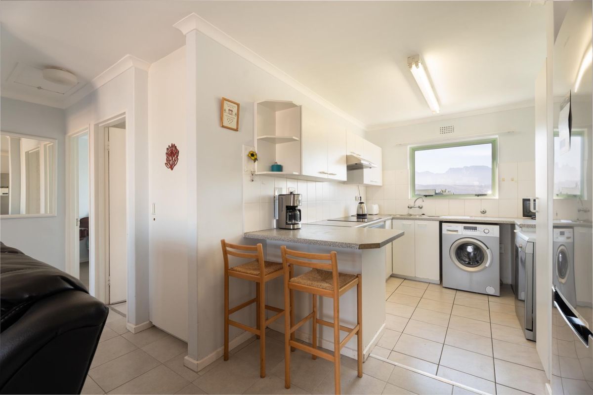 Functional kitchen featuring white cabinetry, tiled flooring, integrated laundry space, and a breakfast bar counter, offering a practical layout for daily living.