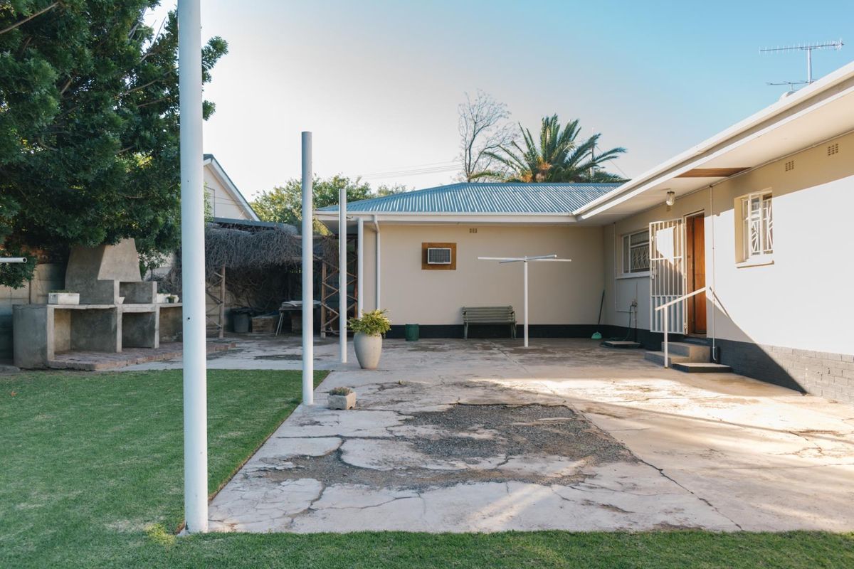Rear exterior view featuring a concrete patio with a built-in braai, lawn area, and direct access to the home via a security gate.