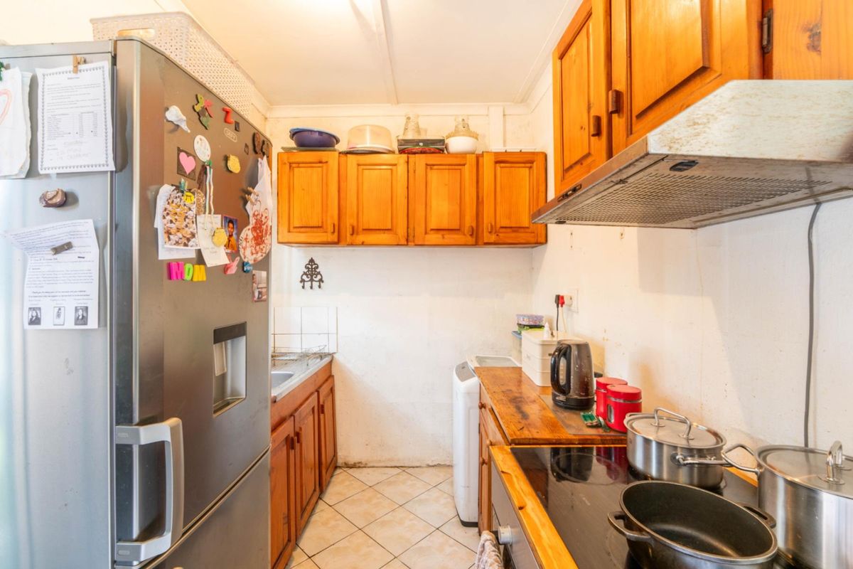 A compact kitchen featuring wooden cabinetry, an electric cooktop with an extractor fan, and tiled flooring, offering potential for a modern renovation.