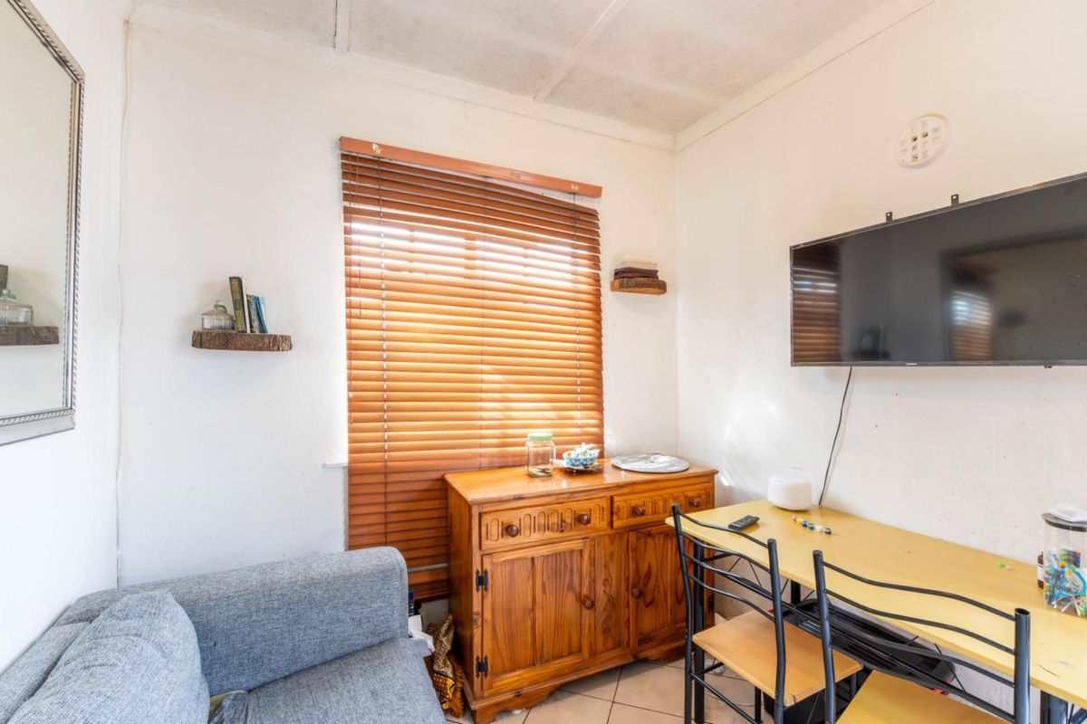 A compact living area featuring tiled flooring, venetian blinds, and wall-mounted television infrastructure, requiring cosmetic updates to the ceiling and wall finishes.